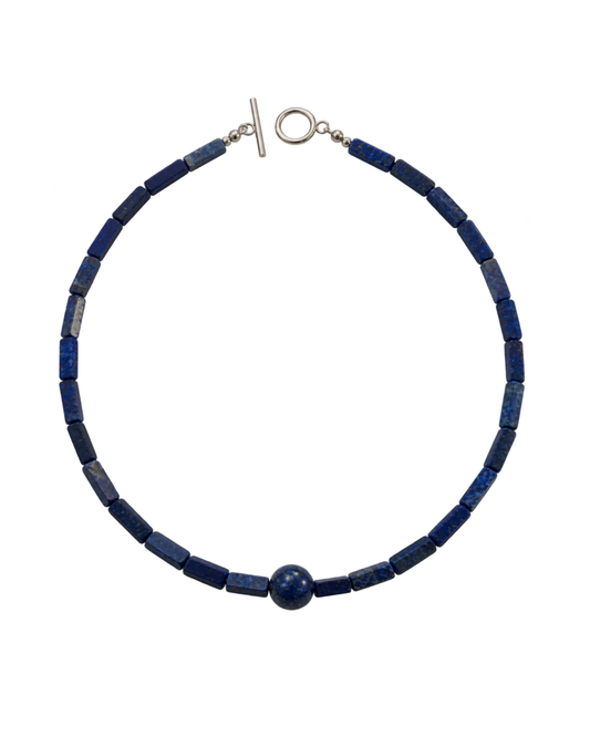 A beaded necklace made of dark blue lapis lazuli cube beads with a single round blue bead at the front, finished with a silver-tone toggle clasp and ring clasp, shown on a plain white background.