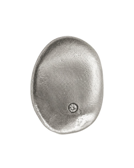 A single metallic oval pendant or medallion in a silver-toned finish, featuring a small circular inset detail near the lower right area, shown on a plain white background.