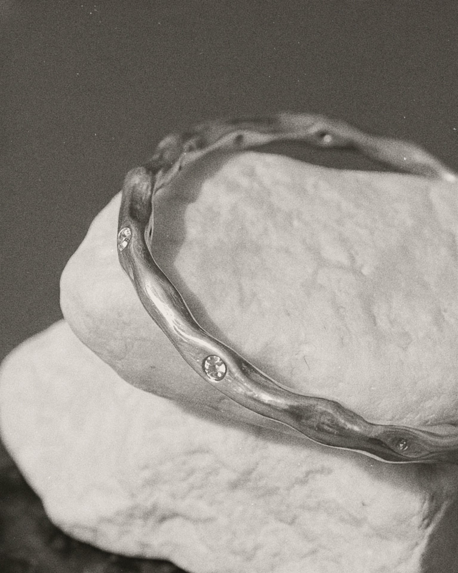 A silver-toned wavy bangle bracelet with small inset stones, displayed on a textured white stone against a dark gray background.